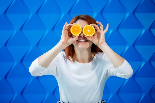 Fille sur fond bleu clair dans un chemisier blanc avec des oranges à la main