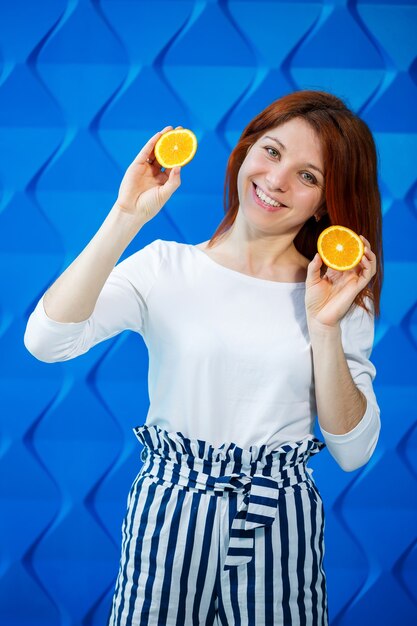 Fille sur fond bleu clair dans un chemisier blanc avec des oranges à la main