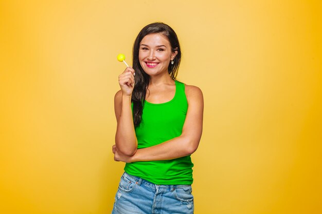 Fille sur fond jaune en t-shirt vert mangeant une sucette