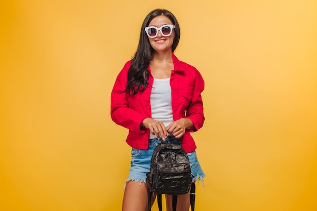 Fille sur fond jaune en veste rouge avec sac à dos