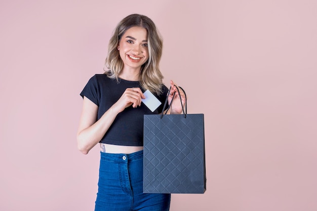 Une fille sur fond rose avec une banque de concept de magasinage de sac en papier noir ou une maquette de carte de réduction