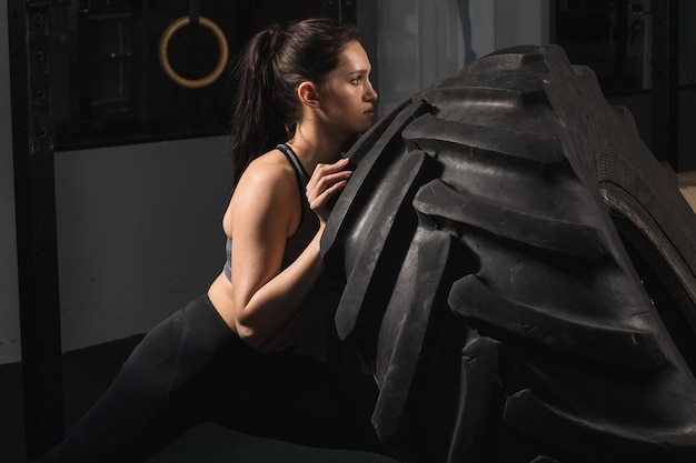 Fille forte renversant un pneu dans la salle de gym.