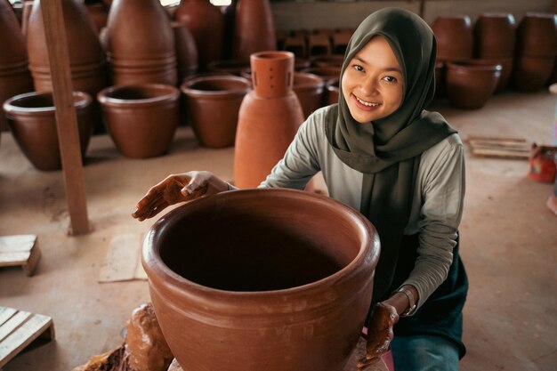 Une fille en foulard sourit en fabriquant des pots en argile sur roues