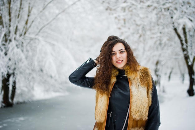 Fille frisée d'élégance en manteau de fourrure au parc forestier enneigé en hiver