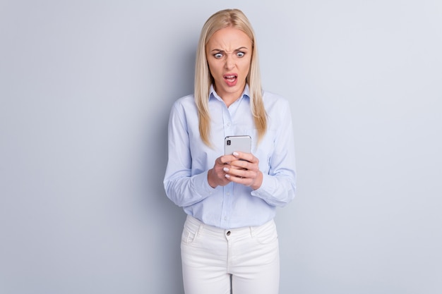 Fille frustrée utilise un écran de look smartphone sur mur gris