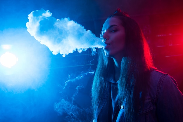 Une fille fume une cigarette et laisse sortir de la fumée dans une discothèque.