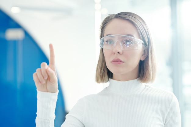 Fille futuriste à l'aide de lunettes intelligentes lors de l'analyse d'informations au bureau