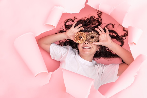 Fille gaie avec des beignets lumineux sur un fond rose de papier