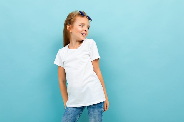 Fille gaie charismatique posant dans un t-shirt blanc sur fond bleu