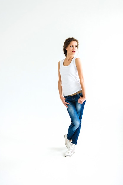 Photo fille gaie dans un t-shirt blanc et un jean bleu foncé en studio sur fond blanc se dresse, s'assoit, court