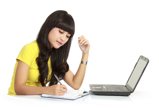 Fille gaie avec ordinateur portable et écrire sur un livre, isolé