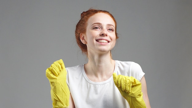 Fille en gants de nettoyage jaunes sur un mur gris