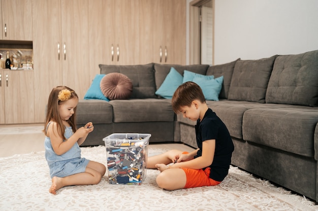 Fille et garçon drôles et mignons jouant au lego à la maison sur le sol, premier mode de vie de rôle d'éducation