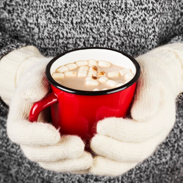 Fille garde une tasse de chocolat chaud avec des guimauves dans des mitaines