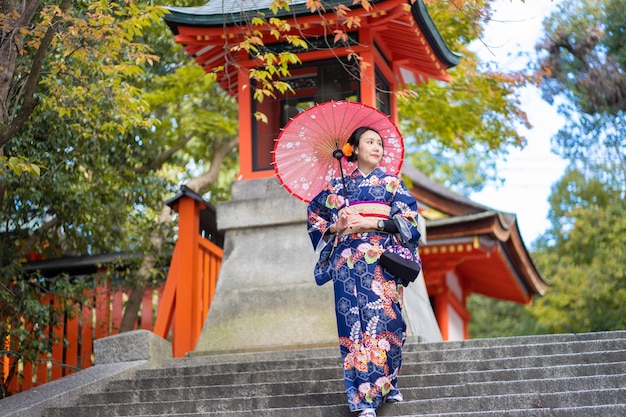 Fille de geishas portant un kimono japonais parmi la porte Tori en bois rouge