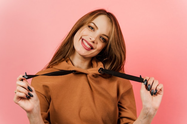 Fille de gestes dans un pull marron sur fond rose