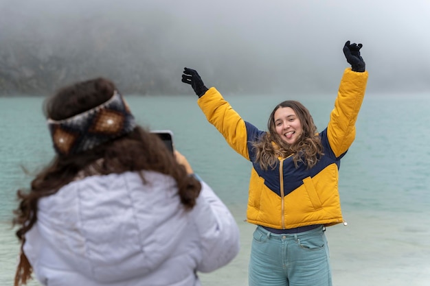Fille gesticulant heureuse pendant qu'un ami prend une photo d'elle devant un lagon