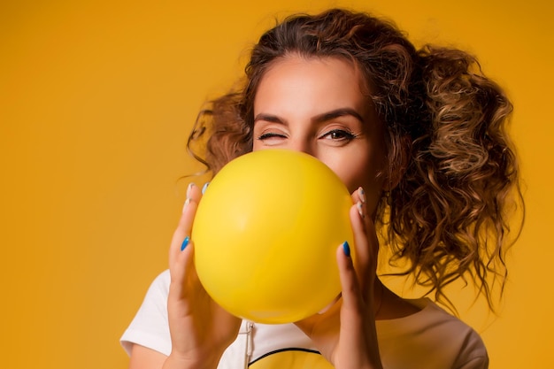 La fille gonfle un ballon sur un fond jaune