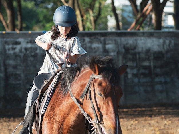 Fille de gosse d'école asiatique à cheval, équitation ou pratique de l'équitation au ranch.