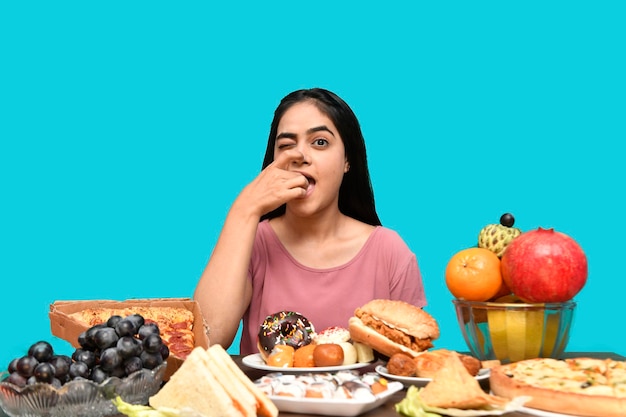 Fille gourmande assise à la table de fruits posant sur fond bleu modèle pakistanais indien