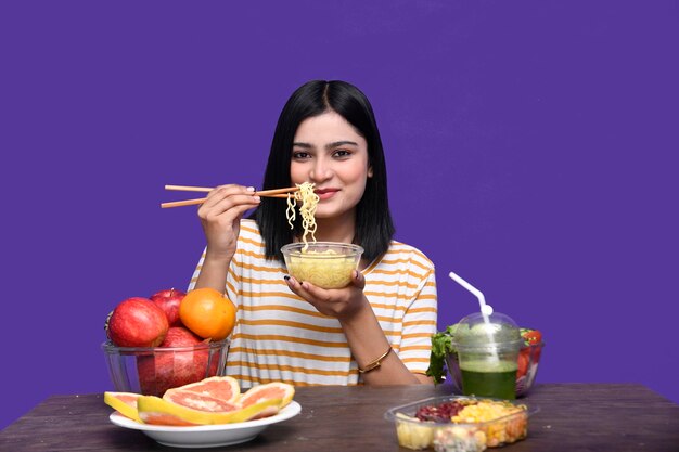 Fille gourmande assise à la table des fruits souriant et tenant un bol de nouilles modèle pakistanais indien