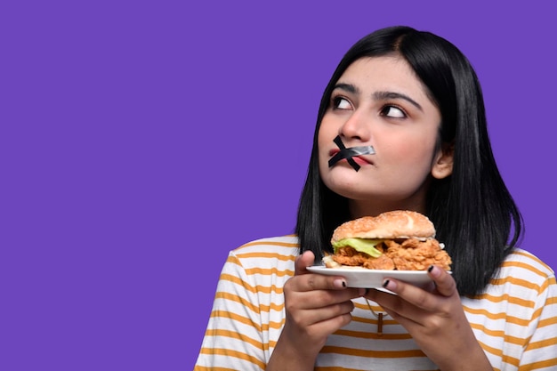 Fille gourmande avec bouche scotchée et tenant un savoureux hamburger à gauche modèle pakistanais indien