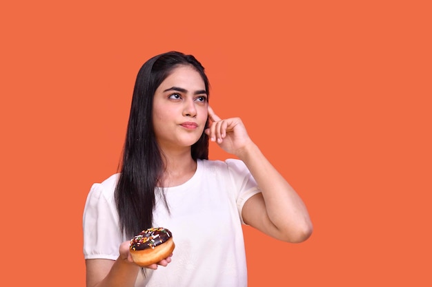 Fille gourmande portant un t-shirt blanc pensant et tenant un beignet au chocolat indien modèle pakistanais