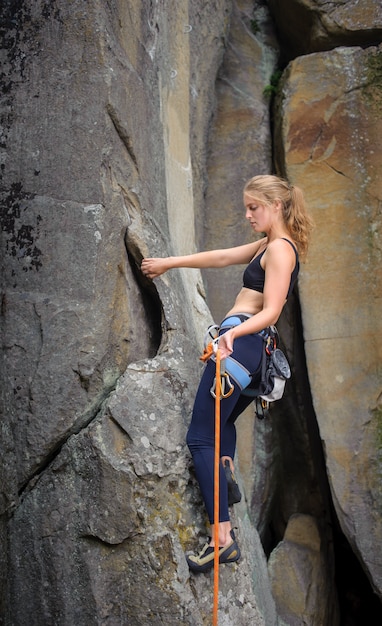 Fille grimpeur grimper avec une corde et des carabines sur un mur rocheux escarpé