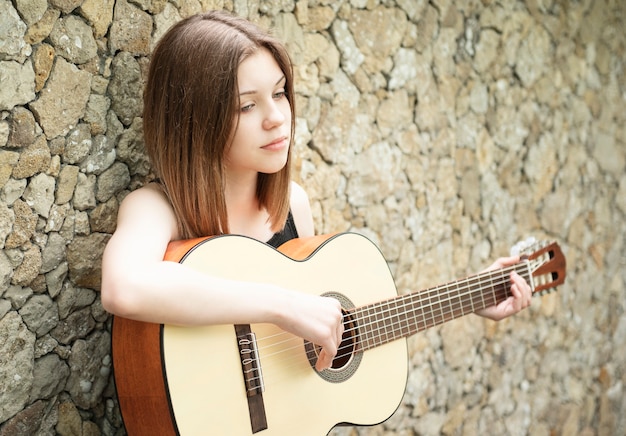 fille avec une guitare contre un mur marron