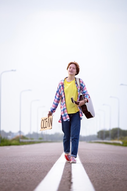 Fille avec une guitare faisant de l'auto-stop