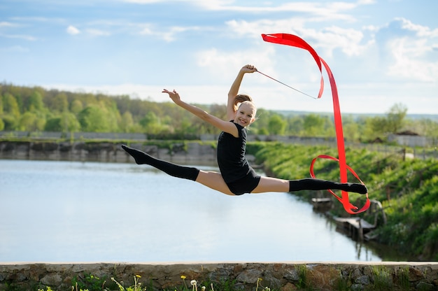 Fille de gymnaste faisant une fente dans un saut avec un ruban