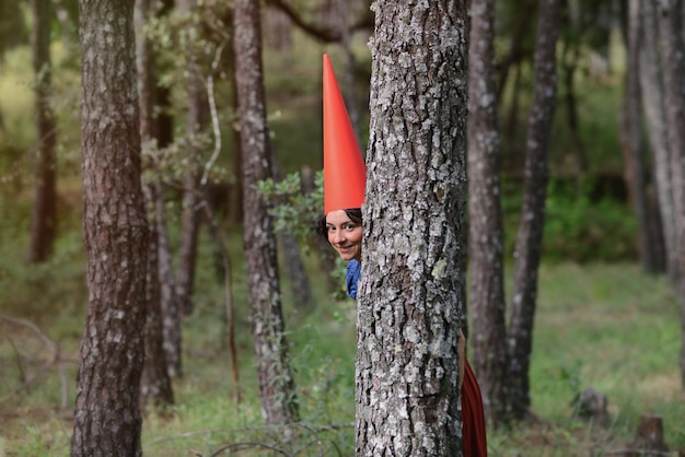 Fille habillée en gnome dans les bois regarde à travers les arbres
