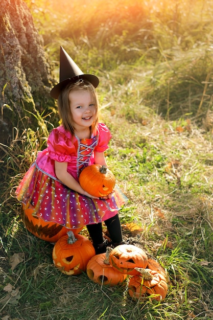Une fille habillée en sorcière est assise avec une citrouille dans les mains à l'Halloween