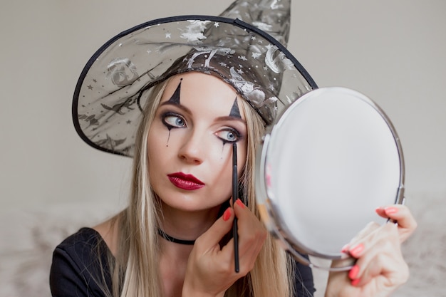 Une fille habillée en sorcière se fait un maquillage d'Halloween