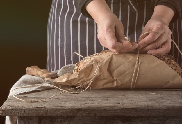 Fille en habits noirs enveloppe une miche de pain en papier kraft brun