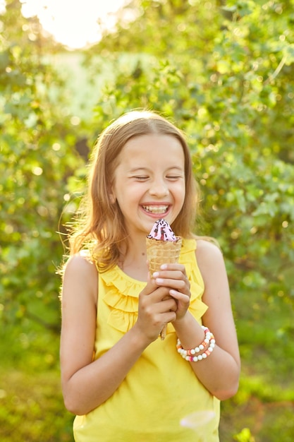 Fille heureuse avec des accolades mangeant un cornet de crème glacée italienne souriant tout en se reposant dans le parc le jour d'été