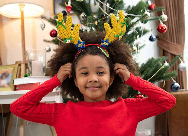 Fille heureuse afro-américaine enfants dans une pièce avec bandeau de renne et décorations de Noël