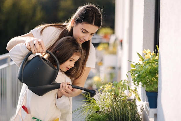 Fille heureuse arrosant les plantes avec sa belle maman Girl39s dans le jardinage global lumineux sur le balcon