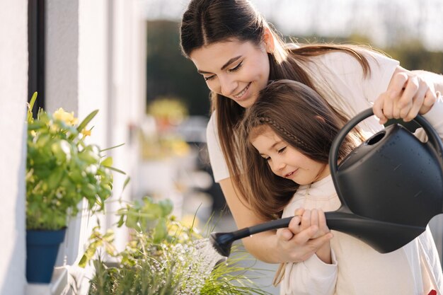 Fille heureuse arrosant des plantes avec sa belle mère filles dans le jardinage général lumineux sur le balcon