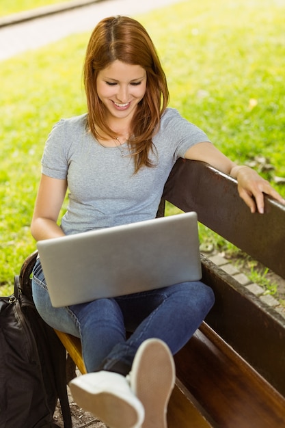 Fille heureuse assis sur un banc en utilisant un ordinateur portable