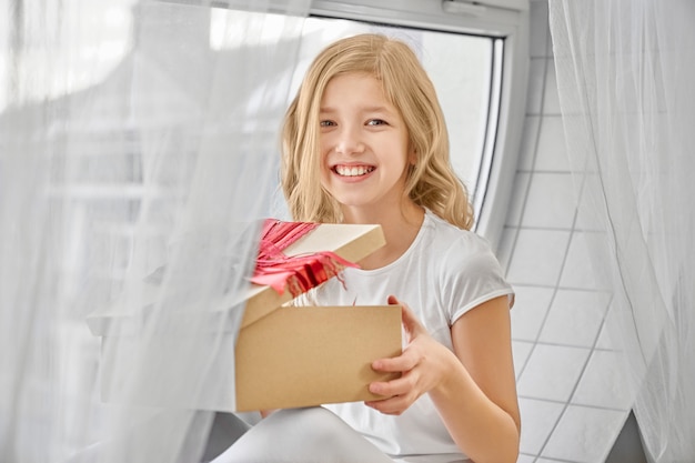 Fille heureuse, assis près de la fenêtre, tenant présent.