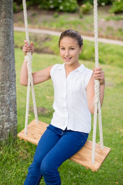 Fille heureuse assise sur une balançoire dans le parc