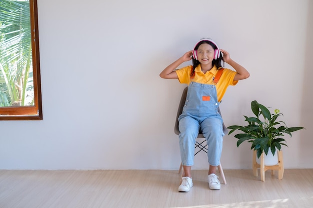 La fille heureuse assise sur une chaise écoutant de la musique dans une pièce minimale à la maison