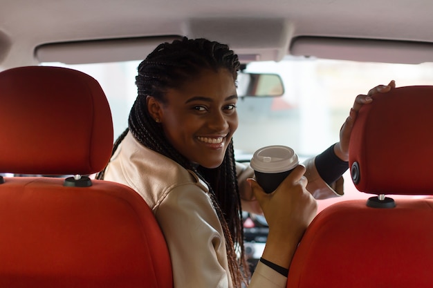 Fille heureuse au volant d'une voiture, boire du café, afro-américain