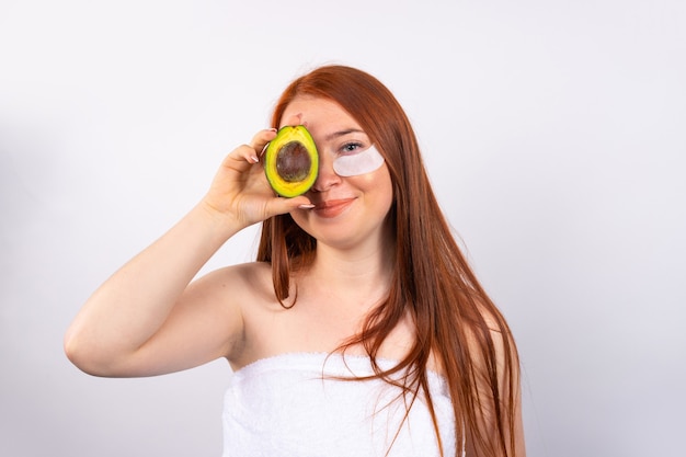 Fille heureuse avec avocat. Photo d'une jeune fille tenant un demi-avocat devant ses yeux et souriant. Concept de santé, beauté, spa et nutrition.