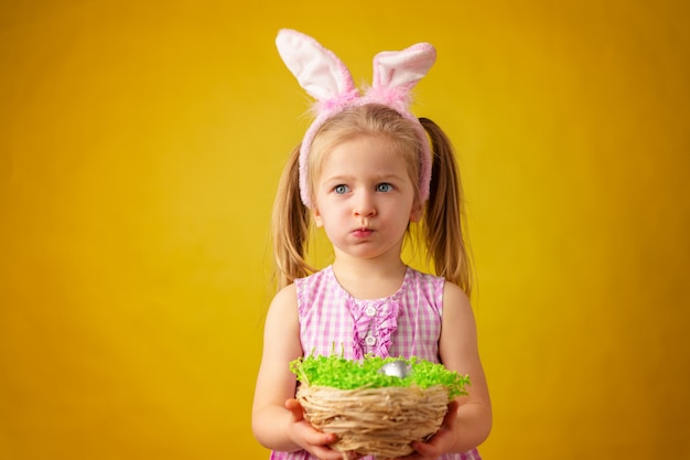 Fille heureuse blonde enfant en bas âge avec des oreilles de lapin et panier d'oeufs pour Pâques