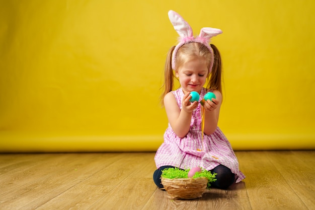 Fille heureuse blonde enfant en bas âge avec des oreilles de lapin et panier d'oeufs pour Pâques