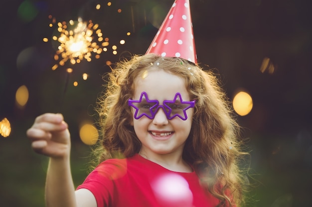 Fille heureuse en chapeau de fête avec sparkler brûlant.