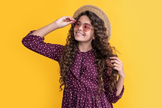 Photo une fille heureuse avec un chapeau de paille et des lunettes de soleil avec de longs cheveux bouclés brunes sur un fond jaune