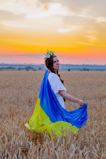 Une fille heureuse en chemise nationale ukrainienne brodée avec une couronne sur la tête tient un grand drapeau jaune-bleu sur fond d'épillets de champ de blé Jour de l'Indépendance Gloire à l'Ukraine Patriotisme